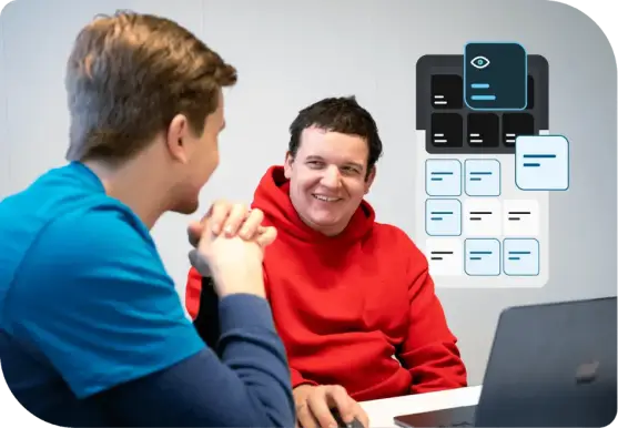 Zwei Personen sitzen an einem Tisch, eine in blauem T-Shirt, die andere in rotem Hoodie; im Hintergrund Illustration des danova Assistant.