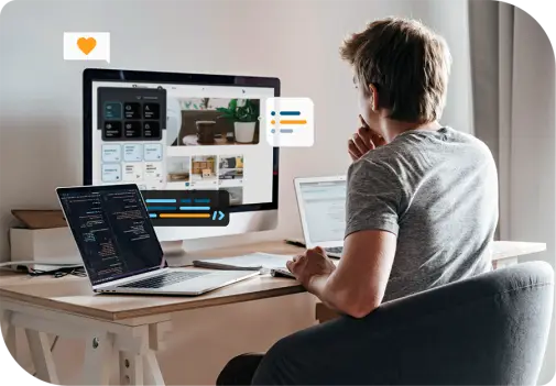 Mann sitzt am Schreibtisch und arbeitet am Computer; auf dem Bildschirm mehrere Fenster mit grafischen Benutzeroberflächen und Texten, daneben ein Laptop mit Code.